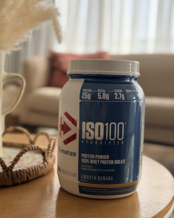 Le pot de Dymatize ISO100 goût Smooth Banana devant le canapé