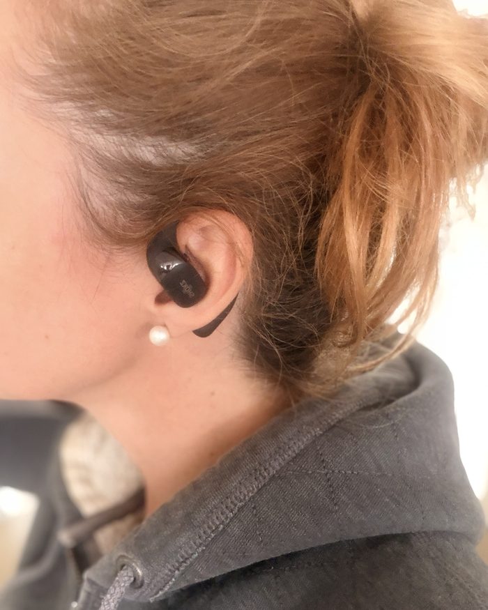 Amélie de profil, un écouteur Shokz OpenFit posé devant l’oreille, le crochet passant derrière