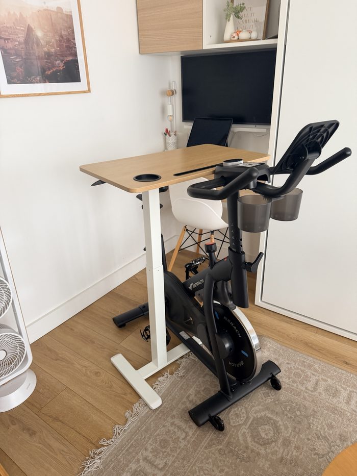 La table haute au plateau en bois et au pied blanc, glissée au-dessus du vélo