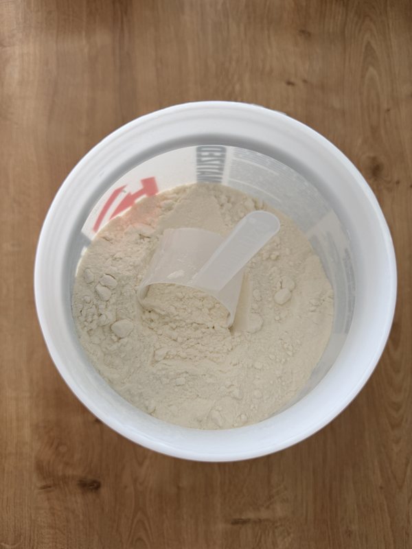 Le pot de whey ouvert vu du dessus, la mesurette plantée dans la poudre