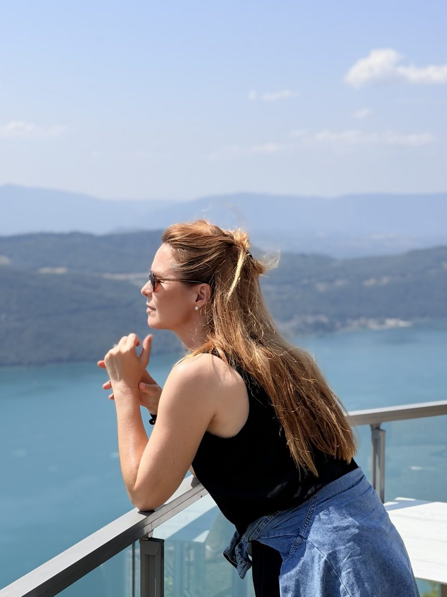 Amélie accoudée à une rambarde vitrée, face au lac du Bourget et aux montagnes