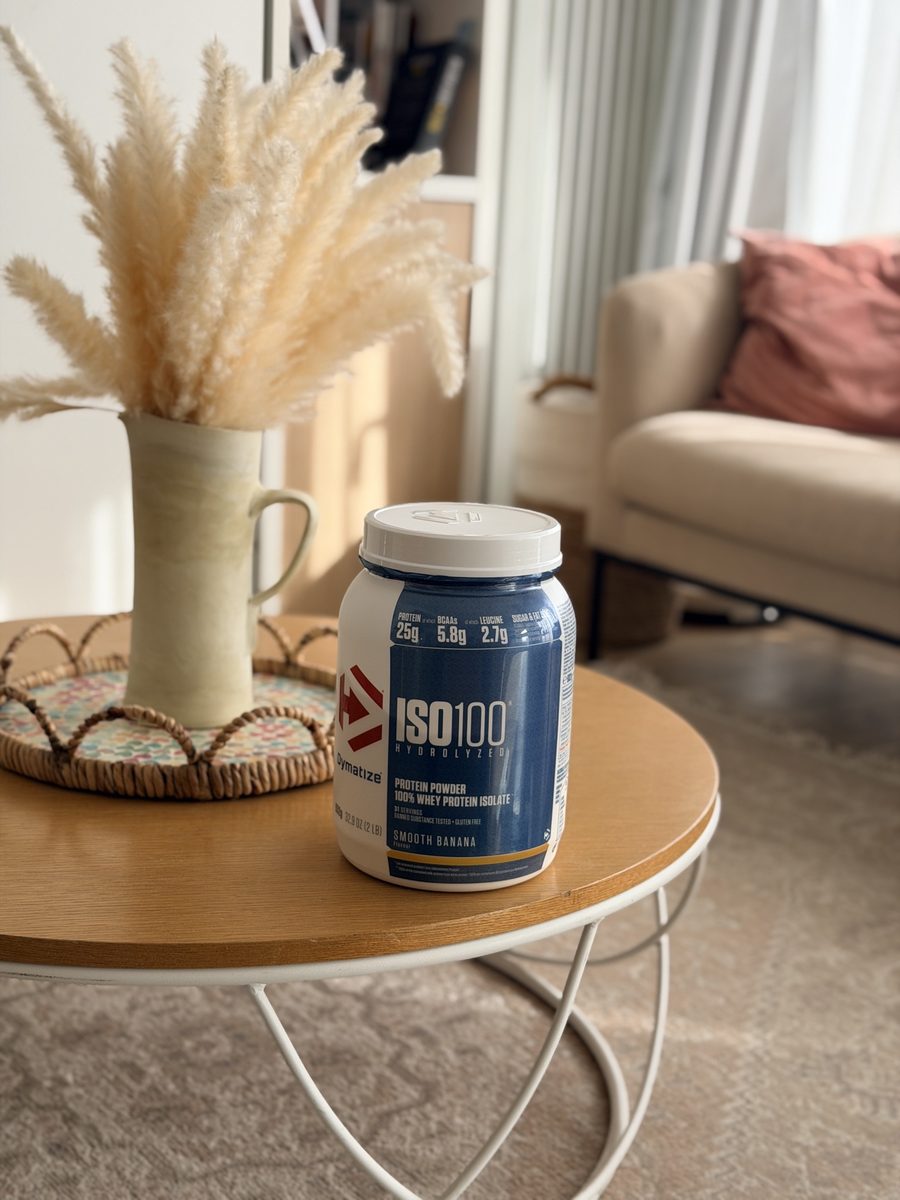 Mon pot de whey Dymatize ISO100 goût banane sur la table basse ronde du salon, devant le canapé
