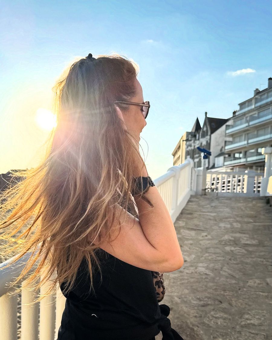 Amélie de dos sur une promenade en bord de mer, cheveux au vent dans le soleil