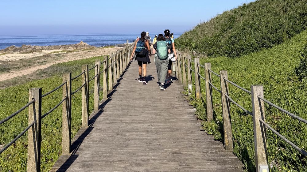 Pèlerins sac au dos sur une passerelle en bois qui mène vers l’océan