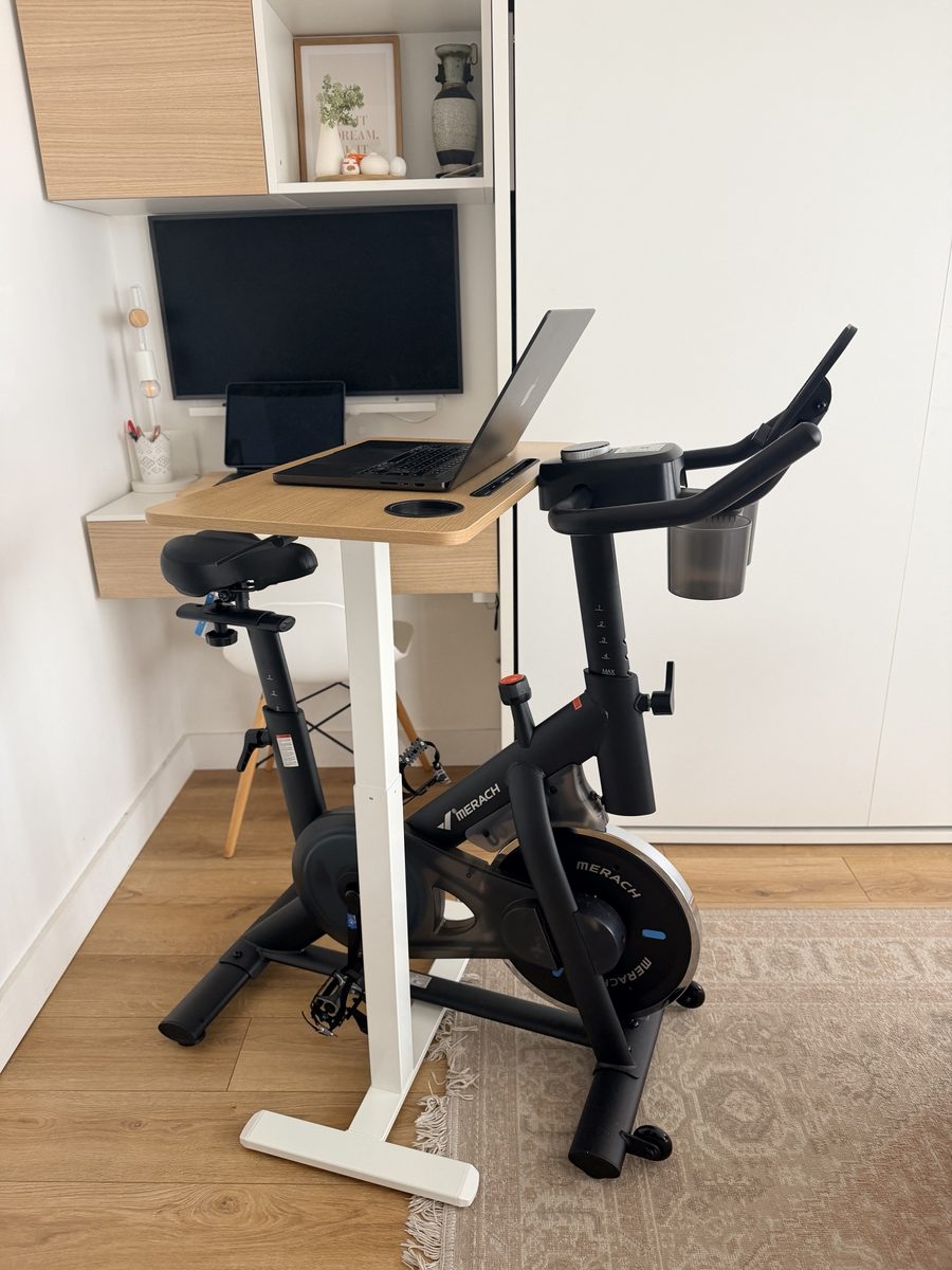 Mon vélo de biking Merach glissé sous ma table haute, MacBook posé dessus, dans mon coin bureau