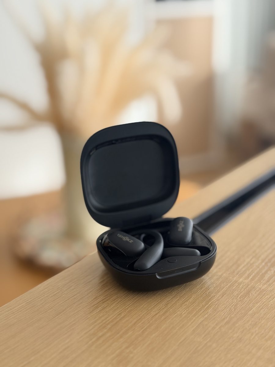 Le boîtier ouvert des écouteurs Shokz OpenFit, posé sur un meuble en bois